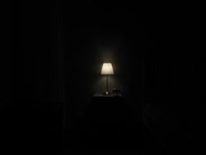 Photo of dark room with small lamp on to show sleeping in a dark room as cure for insomnia. Insomnia treatment available in Houston, Texas 77006.